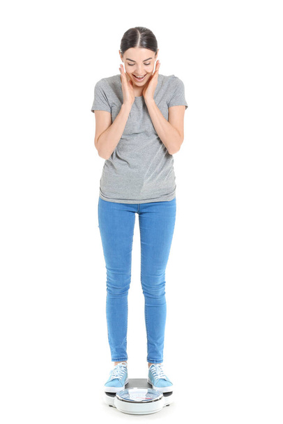Happy young woman standing on scales against white background. Weight loss concept - 写真・画像