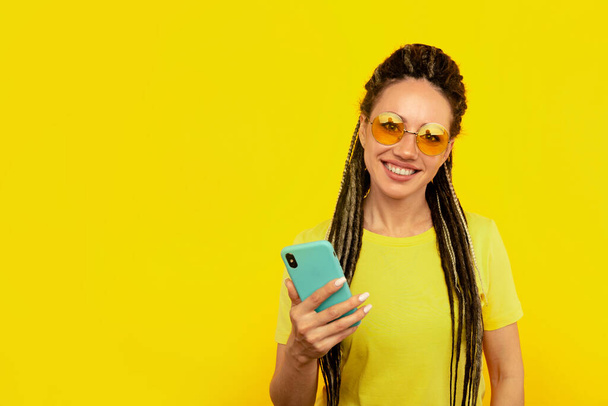 Χαρούμενη χαμογελαστή γυναίκα με φωτεινό τηλέφωνο στο κίτρινο στούντιο. - Φωτογραφία, εικόνα