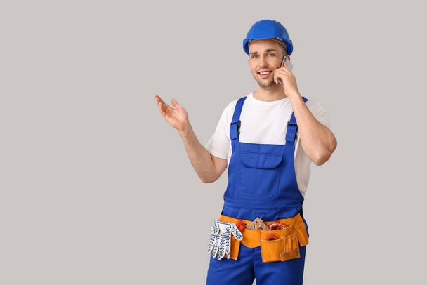 Handsome male worker talking by phone on grey background - Foto, afbeelding
