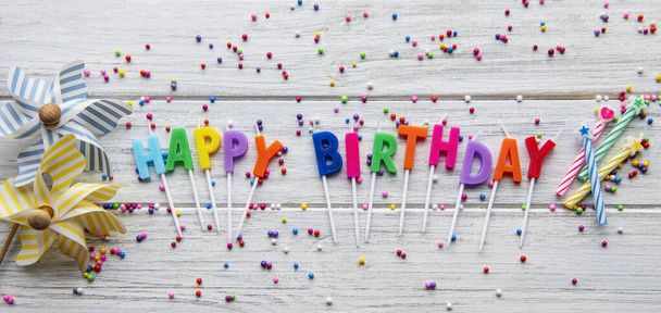 Text Happy Birthday by candle  letters with birthday asseccories, candles and confetti  on white wooden background - Photo, Image