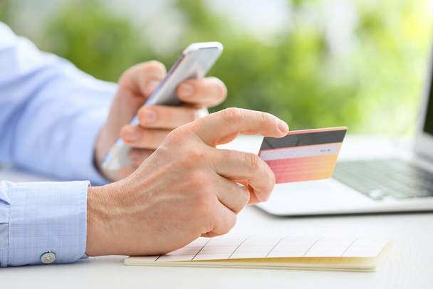 Человек с мобильным телефоном и кредитной картой за столом, крупным планом
 - Фото, изображение
