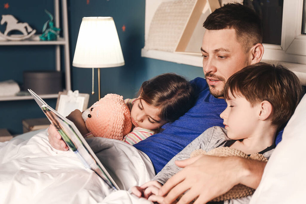 Vater liest seinen kleinen Kindern zu Hause Gute-Nacht-Geschichten vor - Foto, Bild