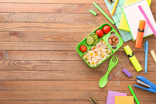 Шкільна обідня коробка зі смачною їжею та канцелярськими товарами на дерев'яному фоні
 - Фото, зображення