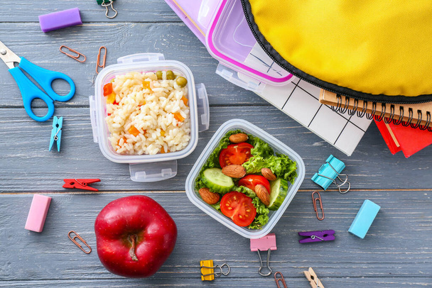 Boîtes à lunch scolaires avec une nourriture savoureuse et de la papeterie sur fond de bois
 - Photo, image