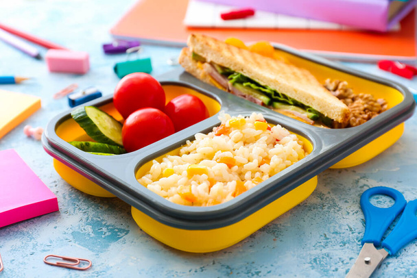 School lunch box with tasty food and stationery on color background - Photo, Image