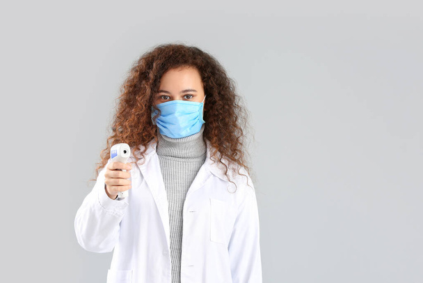 Female doctor with protective mask and thermometer on grey background. Concept of epidemic - Photo, Image