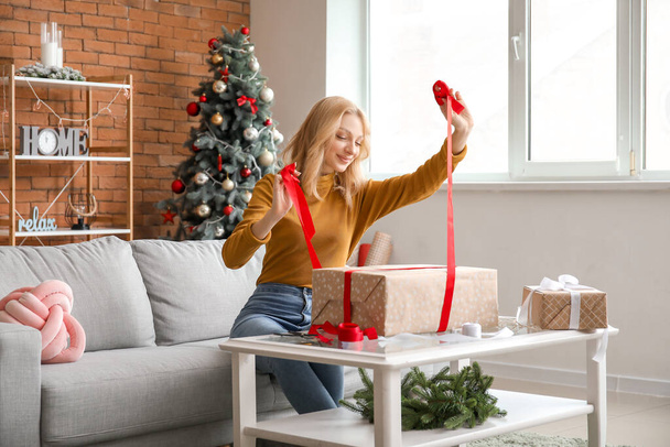 Прекрасна молода жінка обгортає різдвяні подарунки вдома. - Фото, зображення
