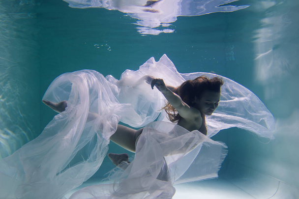 Beautiful girl gymnast and sportswoman swims underwater with shining fabric in the pool	 - Фото, зображення