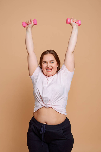 Happy overweight woman doing an exercise, holding small pink dumbbells - Foto, immagini