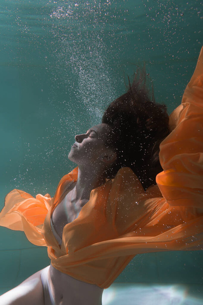 Beautiful girl swims underwater in a yellow dress. 2020 New Year trend Aqua Mente and fatom blue and lush lava. Underwater girl mermaid. Model suitable for advertising - Fotoğraf, Görsel