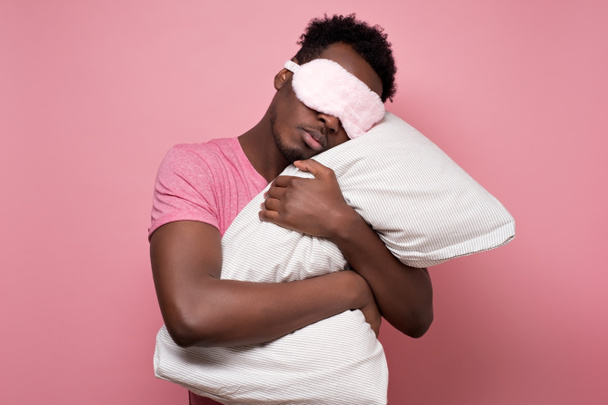 Afrikkalainen amerikkalainen musta mies nukkuu halaamalla tyynyä nukkuva naamio
. - Valokuva, kuva