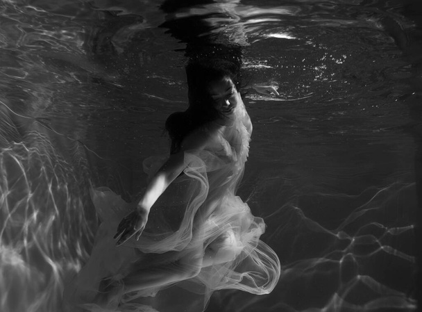 A girl with long dark hair swims underwater in a pink dress and with a crown on her head, like an underwater queen. Fairy tale suitable for advertising - Foto, Imagem