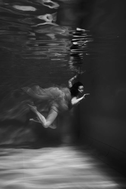 A girl with long dark hair swims underwater in a pink dress and with a crown on her head, like an underwater queen. Fairy tale suitable for advertising - 写真・画像