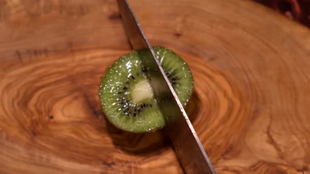cook cuts kiwi with a sharp knife on a wooden Board - Filmati, video