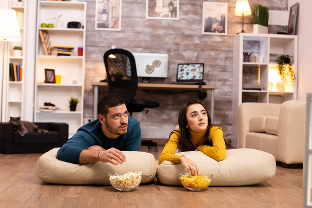 Couple sitting on the floor and watching TV in their living room - Fotoğraf, Görsel