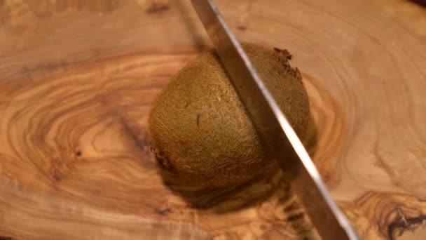 Cocinar cortes kiwi con un cuchillo afilado en una tabla de madera. - Imágenes, Vídeo