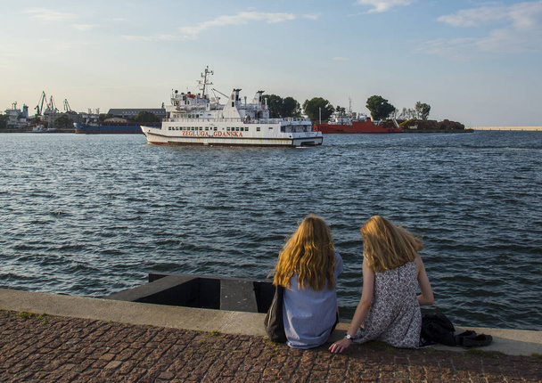 GDYNIA, POMERANIAN VOIVODESHIP / POLAND - JULY 27, 2018: Two girls looking at the Zegluga Gdanska cruise ship going on the Gdynia port waters - 写真・画像