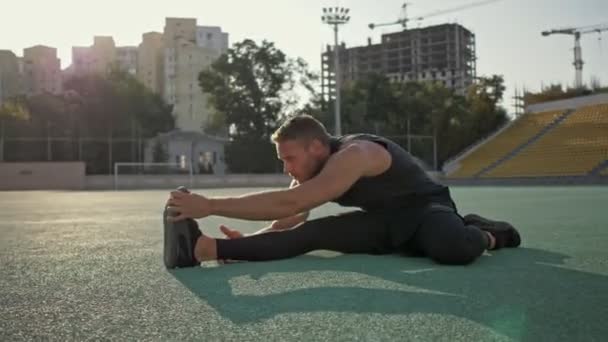 A good-looking young sportsman is going stretching at the stadium - Metraje, vídeo