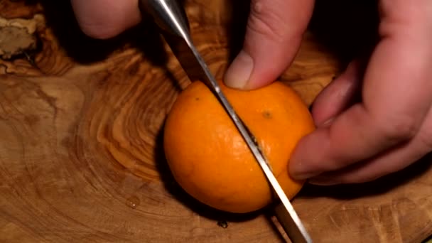 a man cuts a tangerine on a wooden Board with a sharp knife - Filmati, video