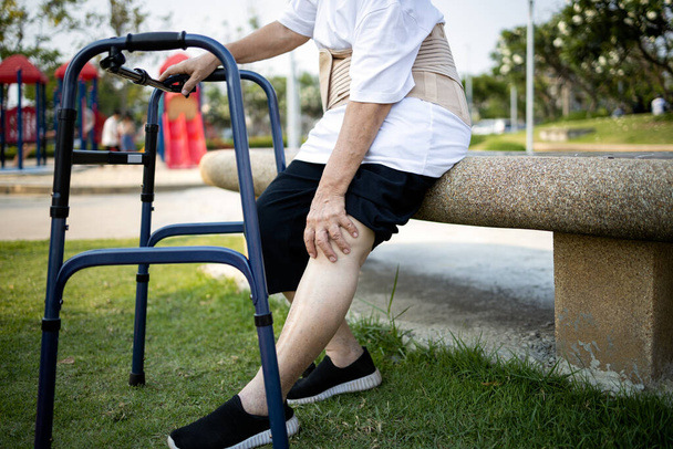 Старша азіатка сидить і масажує коліно, має біль у колінах, жінка похилого віку з гострим болем у колінах, проблеми з кістками, фізичні травми, виснажені старі люди страждають від подагри, артриту, ревматизму. - Фото, зображення