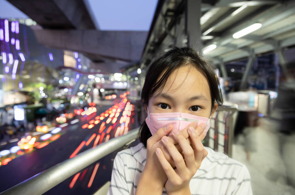 Sairaat aasialaiset yllään suojaava naamio, lapsi tyttö on yskä, tukehtuminen ilmansaasteisiin, myrkyllisen pölyn, savusumun, hienon pölyn, ilman saastumisen tai PM2.5: n ongelmat, ulkona kaupungissa, hengityselinten vaara
 - Valokuva, kuva