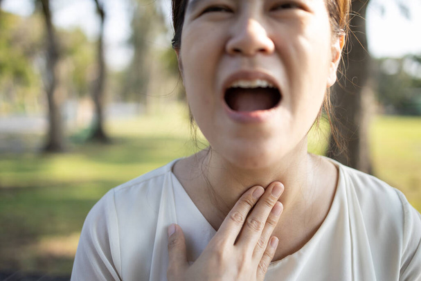 close-up van handen aanraken nek, ziek aziatisch meisje heeft sterke keelpijn, hoest, heesheid, larynx kanker, zwelling, jonge vrouw die lijdt aan keelproblemen, tonsillitis, pijnlijk slikken, gezondheidszorg - Foto, afbeelding