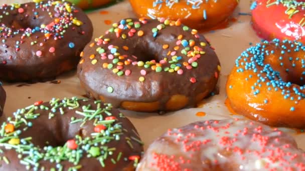 Свежие вкусные круглые пончики с разноцветной глазурью шоколада, розовый, синий, белый, оранжевый, зеленый и различные декоративные порошки лежат в ряд на столе
 - Кадры, видео