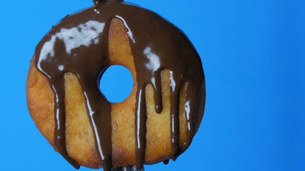 Большой круглый пончик на вилке, на которой шоколадная глазурь течет на голубом фоне
 - Кадры, видео