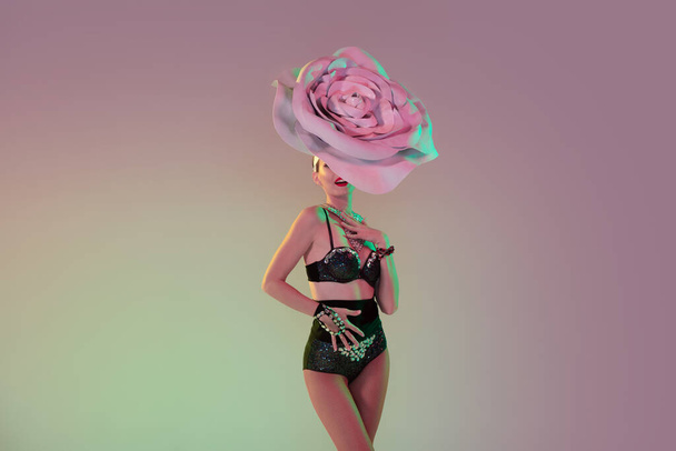 Young female dancer with huge floral hats in neon light on gradient background - Photo, image