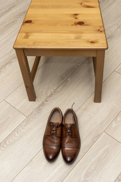 Classic men's shoes with laces near wooden chair on wooden floor, vertical - Photo, Image