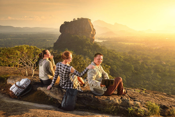 Gruppo giovani turisti si rilassa e guarda durante le vacanze colorato tramonto sullo sfondo del famoso altopiano roccioso picco del Leone, Sigiriya. Sri Lanka
 - Foto, immagini
