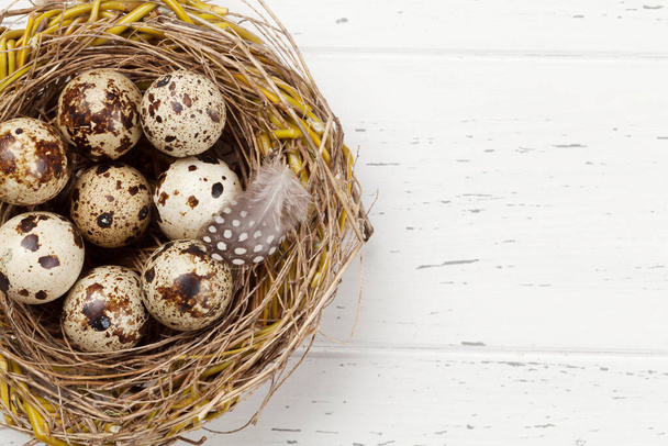 Tarjeta de felicitación de Pascua con huevos de codorniz en nido sobre fondo de madera. Vista superior plano con espacio para sus saludos
 - Foto, imagen