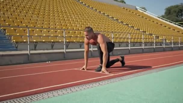 A serious young shirtless sportsman is beginning to run while training for the marathon at the stadium - 映像、動画
