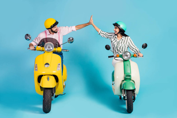 Full size photo of funny two people lady guy drive retro moped one team travelers good mood clap arms formalwear clothes protective caps isolated blue color background - Photo, Image
