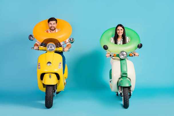 Full body photo of funky two people lady guy drive retro moped good mood hold colorful life buoys travelers resort vacation formalwear clothes isolated blue color background - Valokuva, kuva