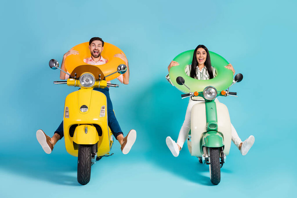 Full length photo of funky two people lady guy drive retro moped good mood spread legs crazy hold colorful life buoys travelers formalwear clothes isolated blue color background - Fotó, kép