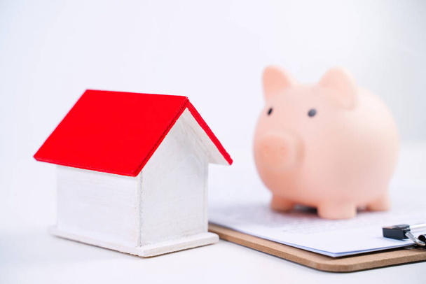 Financial concpet - Piggy bank, beautiful red white wooden house model on white background, saving money to buy insurance, close up, copy space. - Foto, afbeelding