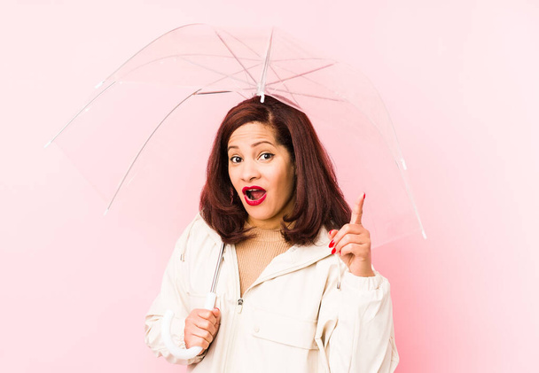Mujer latina de mediana edad usando un paraguas aislado teniendo una idea, concepto de inspiración
. - Foto, Imagen