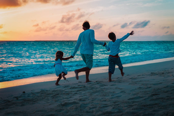 Отец и двое детей играют на пляже на закате
 - Фото, изображение