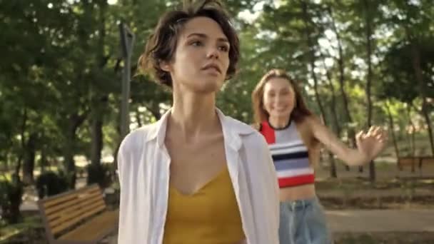 A beautiful young girl is running to hug her friend in the city park - Materiał filmowy, wideo