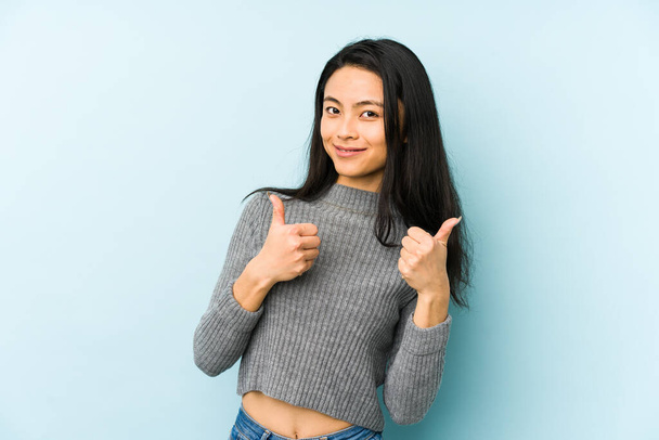 Mulher chinesa jovem isolado em um fundo azul levantando os dois polegares para cima, sorrindo e confiante
. - Foto, Imagem