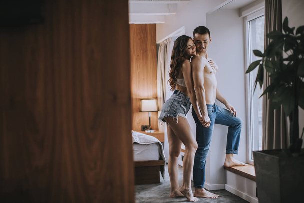 Affectueux jeune couple debout par la fenêtre dans la chambre de l'appartement - Photo, image