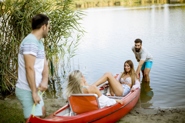 Handsome young men pulling canoe with young women into calm lake - Foto, Bild