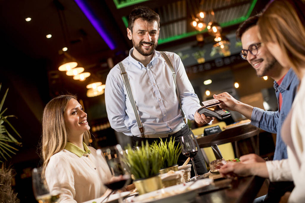 Mladý muž platí bezkontaktní kreditní kartou v restauraci po večeři - Fotografie, Obrázek