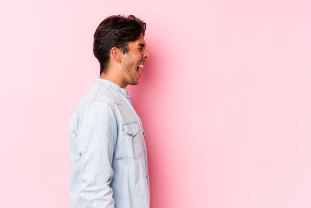 Νεαρός καυκάσιος άνδρας ποζάρει σε ροζ φόντο απομονωμένος φωνάζοντας προς ένα χώρο αντιγραφής - Φωτογραφία, εικόνα