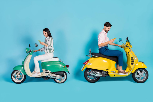 Full length profile side photo of positive two people bikers driver drive yellow green choppers use cellphone search gps location wear trousers shirt isolated blue color background - Photo, Image