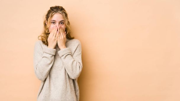 Young caucasian woman isolated on beige background laughing about something, covering mouth with hands. - Foto, imagen