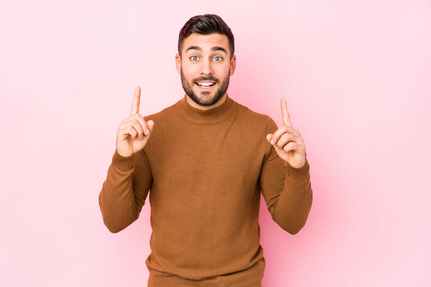 Joven hombre caucásico sobre un fondo rosa aislado indica con ambos dedos delanteros hacia arriba mostrando un espacio en blanco
. - Foto, imagen