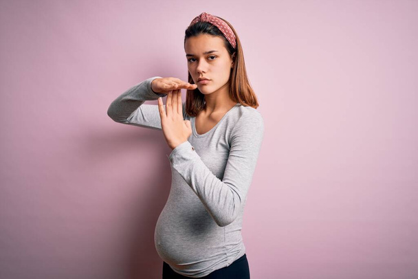 Nuori kaunis teini tyttö raskaana odottaa vauva yli eristetty vaaleanpunainen tausta Doing aikalisä ele kädet, turhautunut ja vakava kasvot
 - Valokuva, kuva