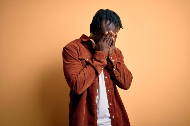 Young handsome african american man wearing casual jacket standing over yellow background with sad expression covering face with hands while crying. Depression concept. - Photo, Image